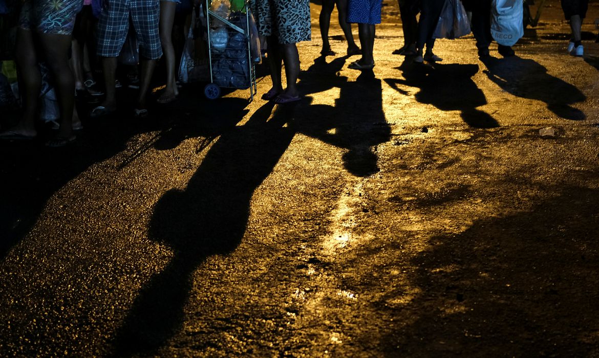 As pessoas esperam na fila para receber peixes doados por um vendedor de peixes depois de terminar seu dia de vendas no centro de abastecimento do Rio de Janeiro (CEASA) durante o surto de doença por coronavírus (COVID-19), no Rio de Janeiro