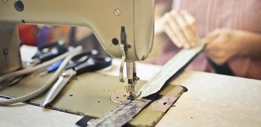 Detalhe de máquina de costurar; mulher trabalha em tira de tecido