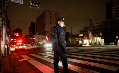 Policial organiza o tráfego de veículos em rua de Tóquio após terremoto cortar energia