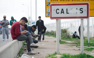 Refugiados mandam mensagens próximos ao Porto de Calais, onde um acampamento abriga cerca de 1,5 mil migrantes