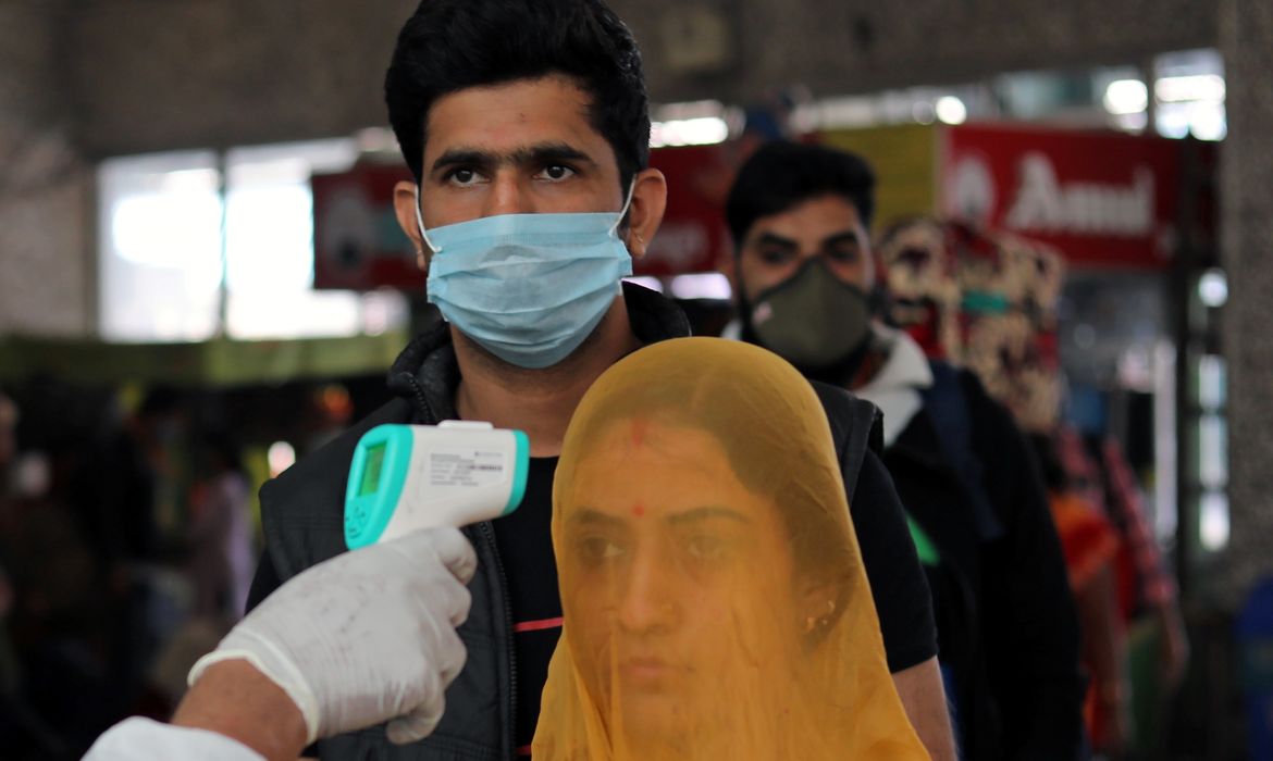 Um trabalhador de saúde em equipamentos de proteção individual (EPI) verifica a temperatura dos passageiros em meio à propagação da doença coronavírus (COVID-19), em uma estação ferroviária em Mumbai, Índia, 19 de dezembro de 2020. REUTERS / Fr