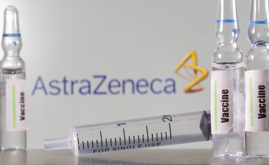 um tubo de ensaio etiquetado com a vacina é visto na frente do logotipo da AstraZeneca