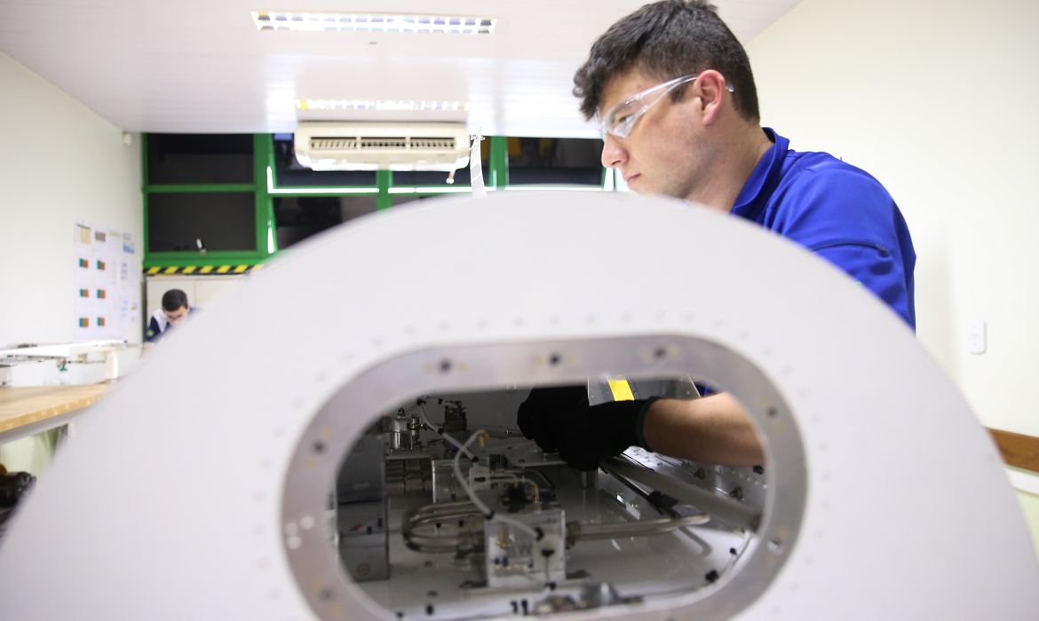Estudante de educação profissional realiza atividade prática em laboratório técnico, operando equipamento industrial durante curso de formação tecnológica.