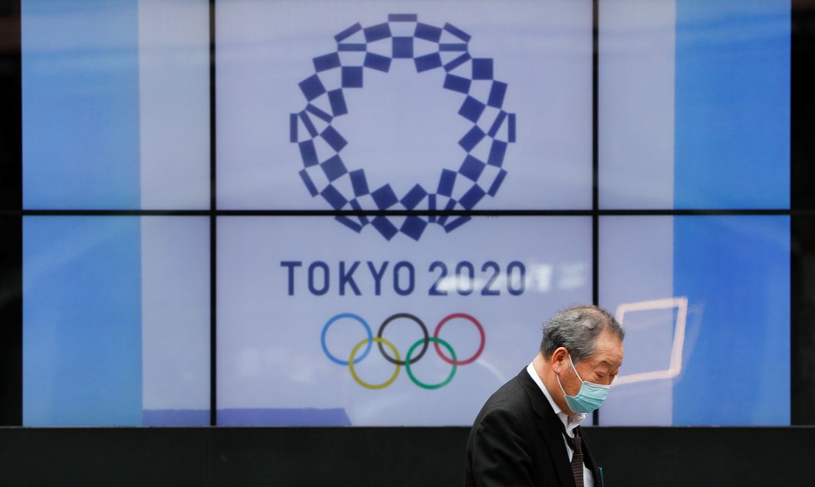 Transeunte com máscara de proteção passa em frente ao logo da Olimpíada Tóquio-2020 em Tóquio - anéis 