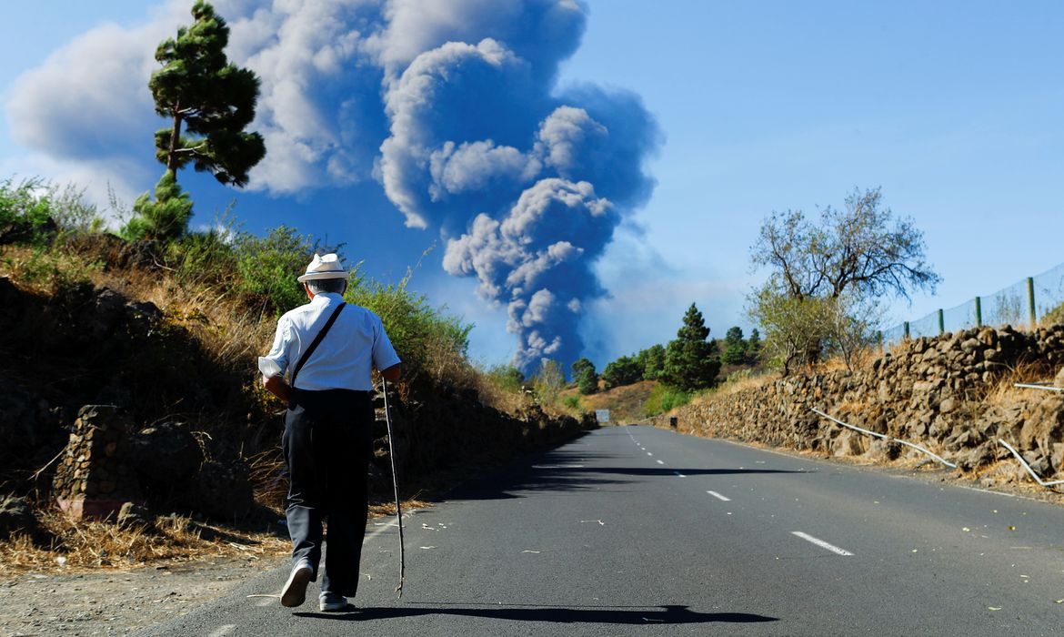 A man walks along an El Paso road while observing a large ash column from the Cumbre Vieja volcano on the Canary Island of La Palma