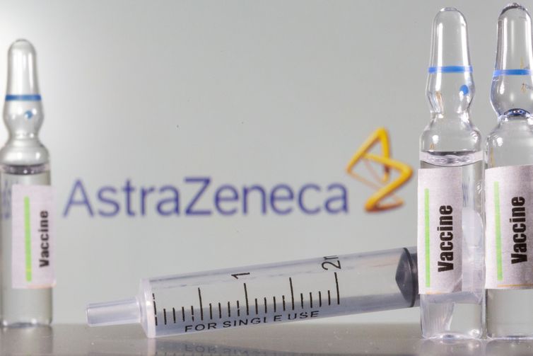 um tubo de ensaio etiquetado com a vacina é visto na frente do logotipo da AstraZeneca