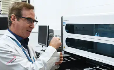 Brasília (DF), 29/10/2024 - Médico e pesquisador Júlio Teixeira ao lado de equipamento usado em teste DNA-HPV. Foto: Roche/Divulgação