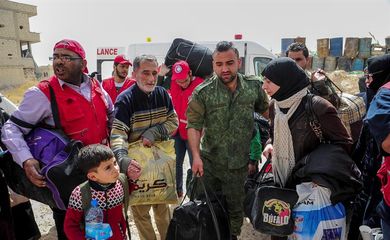 Empregados do Crescente Vermelho (versão árabe da Cruz Vernelha) ajudam civis a deixar a área de Duma, em Ghouta Oriental, na Síria, ainda sob controle dos rebeldes. Foto da Agência de Notícias Árabe-Síria (Sana)