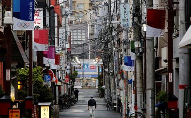 Homem com máscara de proteção caminha em rua comercial decorada com bandeiras da Olimpíada Tóquio 2020 em Tóquio - anéis - rua