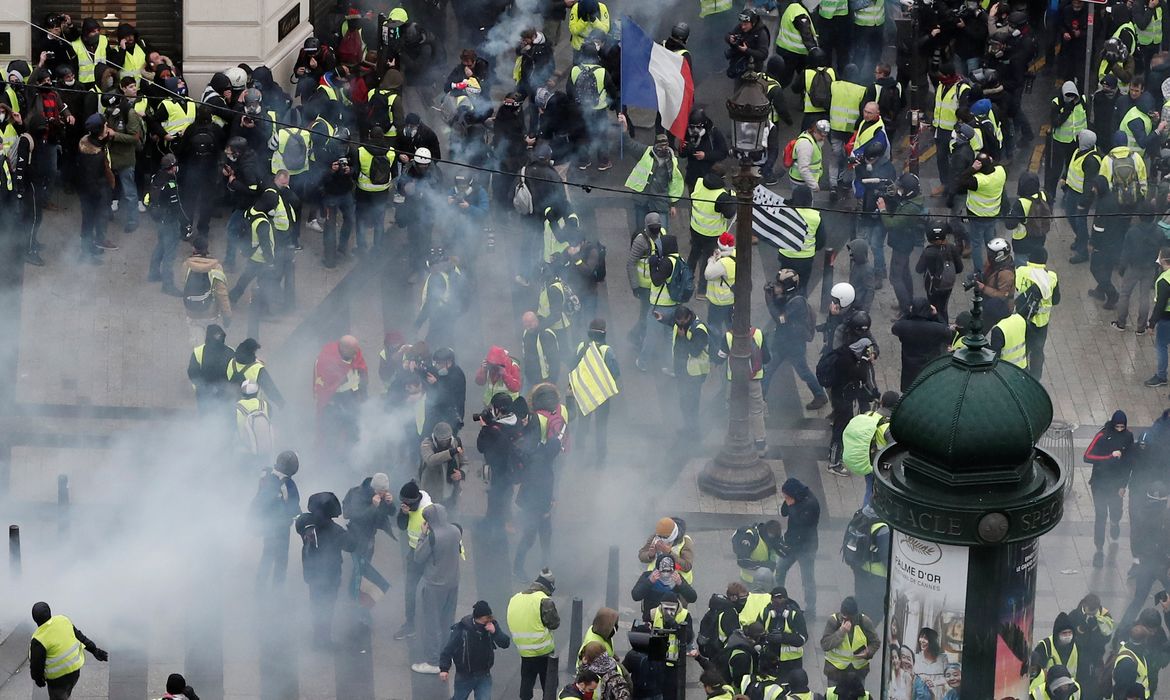 Tear gars floats in the air around protesters wearing yellow vests during clashes with French Gendarmes on the Champs-Elysees Avenue as part of a demonstration by the 