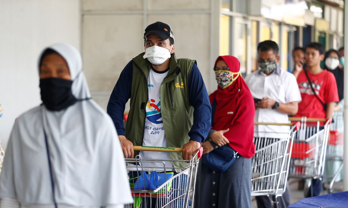 Consumidores com máscaras protetoras alinham-se diante de um mercado em meio ao surto de doença por coronavírus (COVID-19)