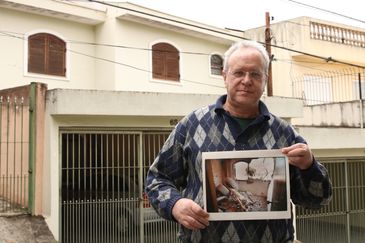 O jornalista Jorge Tadeu da Silva, um dos afetados pelo acidente com o avião modelo Fokker 100 da TAM que vitmou 99 pessoas em 1996, segura foto de como ficou a casa dele na rua Luís Orsini de Castro, no Jabaquara.