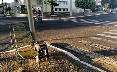 Rua remota durante a pandemia. 
No primeiro plano da foto, cadeira de balanço e faixas de pedestre. Ao fundo, ciclista solitário em uma rua vazia.