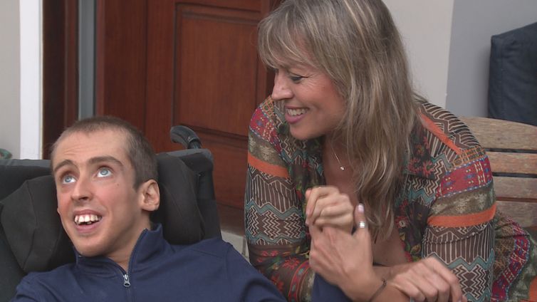 Sala. Nicolás em uma cadeira de rodas. Sentada ao lado, Teresa segura a mão esquerda do filho.  