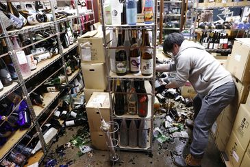 A worker cleans up broken bottles at a liquor shop after a strong quake in Fukushima