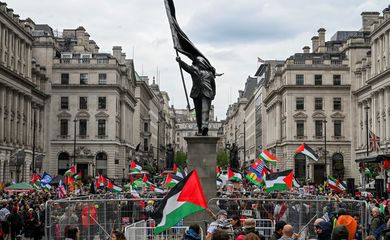 Pessoas seguram bandeiras palestinas ao lado de uma estátua, representando uma figura carregando uma bandeira cobrindo o rosto e descendo de um pedestal, do artista de rua britânico Banksy, durante uma marcha, realizada pela Palestine Solidarity Campaign, para marcar o 78º aniversário da Nakba e contra o comício 