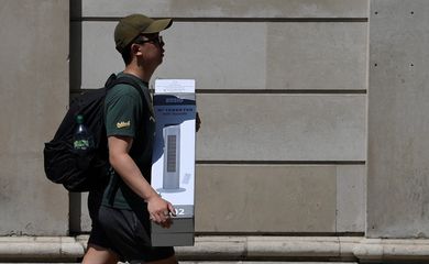 A man carries a fan during the hot weather in the City of London financial district, London