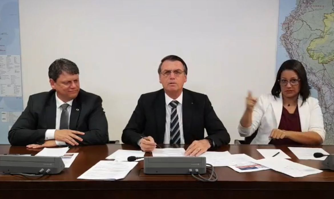 O presidente Jair Bolsonaro faz transmissão ao vivo ao lado do ministro da Infraestrutura, Tarcísio Gomes de Freitas, e da intérprete de libras, Elizângela Castelo Branco.