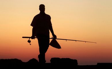 Homem carrega vara de pescar durante pôr do sol ao longo da costa na cidade mediterrânea de Alexandria