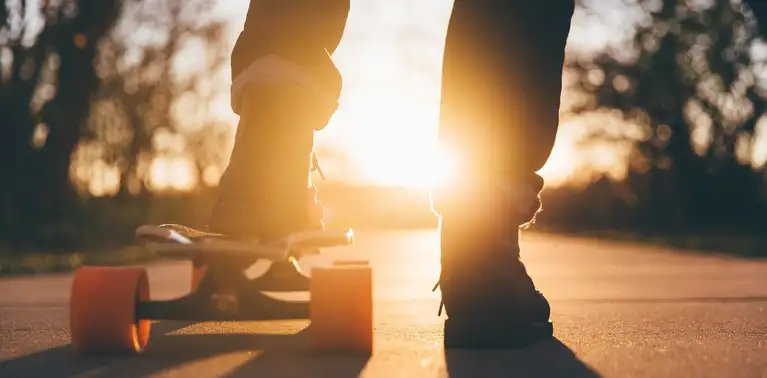 Close de pés de jovem sobre skate com o sol no horizonte
