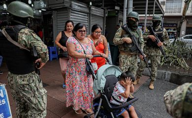 People walk past armed soldiers, as they guard a commercial area, in the aftermath of a wave a violence that saw the storming of a TV station on-air and explosions around the nation, in Quito, Ecuador, January 11, 2024. REUTERS/Ivan Alvarado