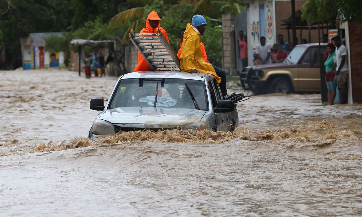 Um grupo de pessoas tenta cruzar uma via alagada in Leogane, no Haiti, após a passagem do Furacão Matthew. O país já registrou 21 mortes em decorrência do furacão