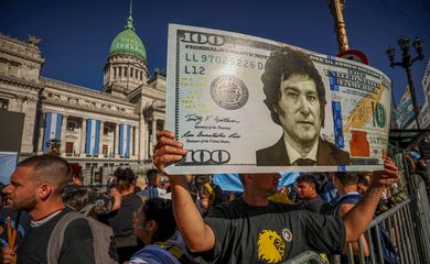 A supporter of Argentina's President-elect Javier Milei holds up a representation of a 100 dollar bill featuring an image of c on the day of his swearing-in ceremony, outside the National Congress, in Buenos Aires, Argentina December 10, 2023. REUTERS/Agustin Marcarian
