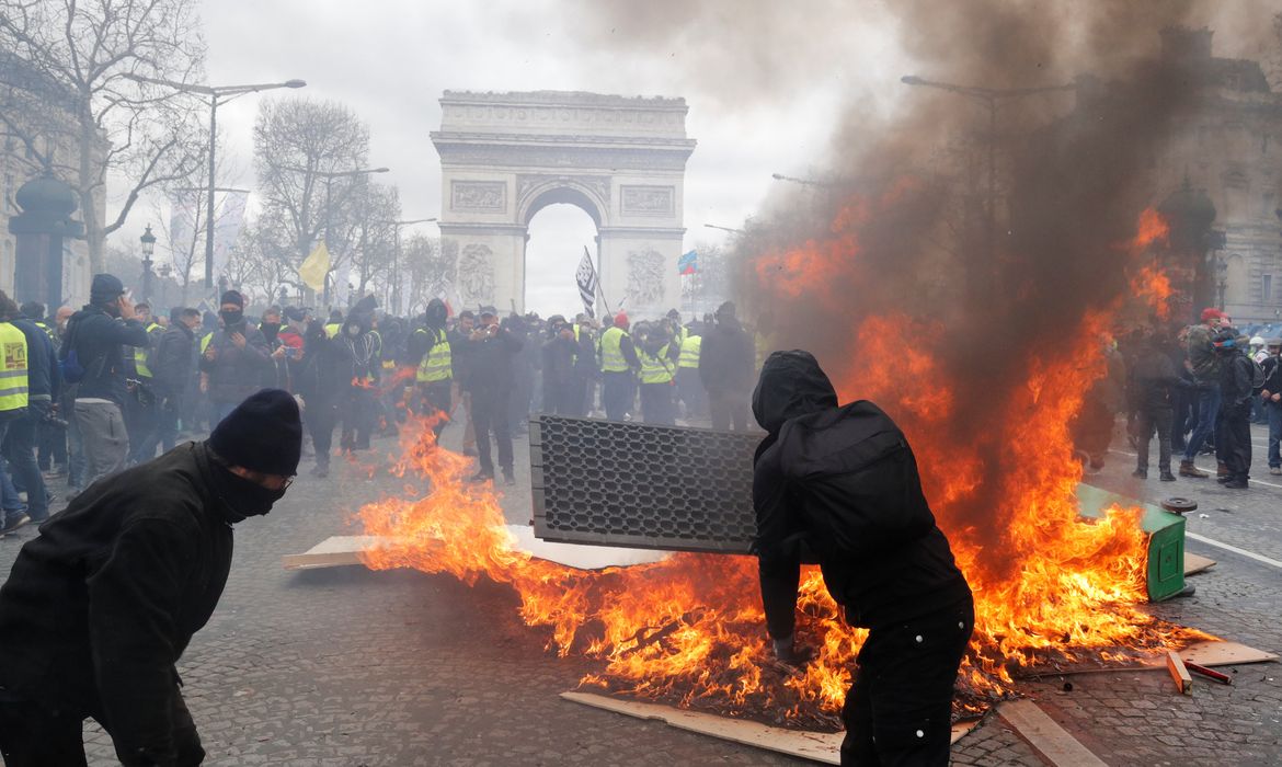 Os manifestantes reagem ao lado de uma barricada em chamas, durante uma demonstração do movimento 