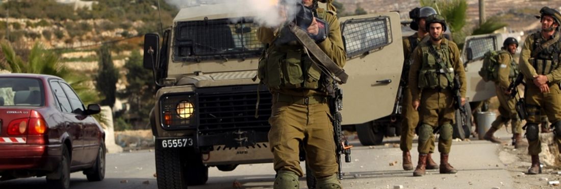 Soldado israelense atira bomba de gás lacrimogêneo em manifestantes palestinos em Bet Omar, na Cisjordânia, durante protesto contra operação militar de Israel na Faixa de Gaza