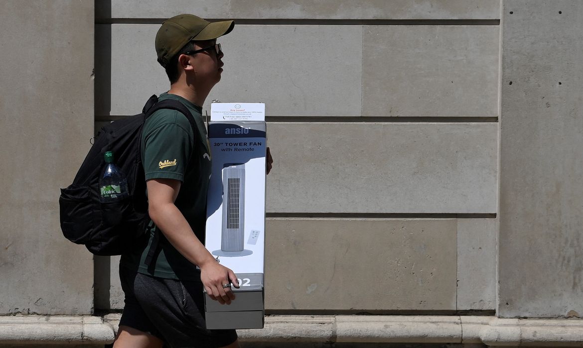 A man carries a fan during the hot weather in the City of London financial district, London