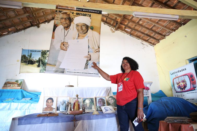 Quilombola Sandra Braga, 50 anos, ao lado do poster dos avós com o documento de certificação da terra nas mãos.