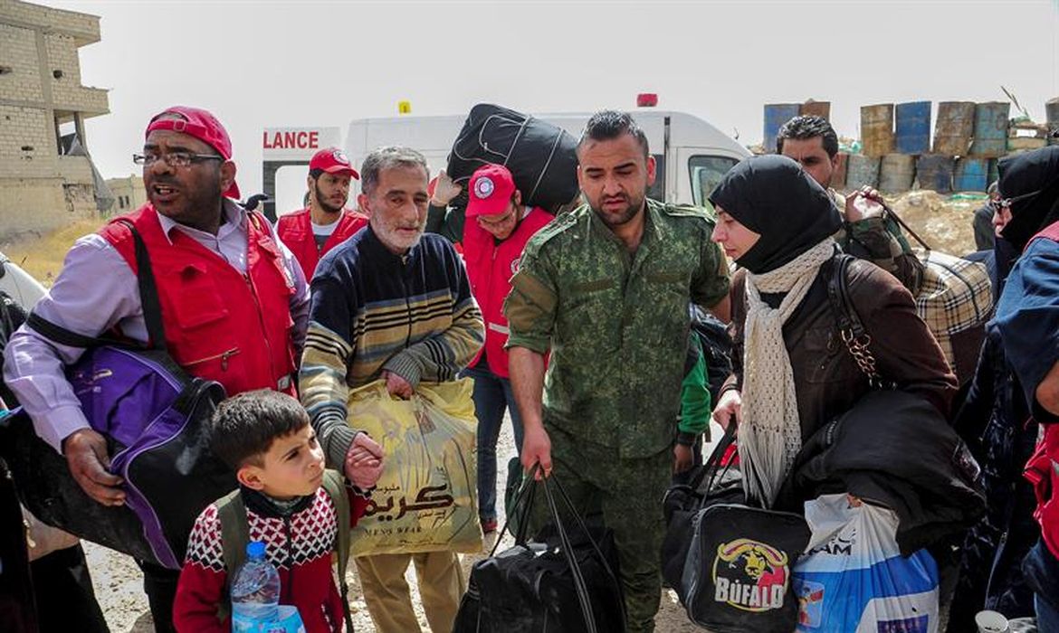 Empregados do Crescente Vermelho (versão árabe da Cruz Vernelha) ajudam civis a deixar a área de Duma, em Ghouta Oriental, na Síria, ainda sob controle dos rebeldes. Foto da Agência de Notícias Árabe-Síria (Sana)