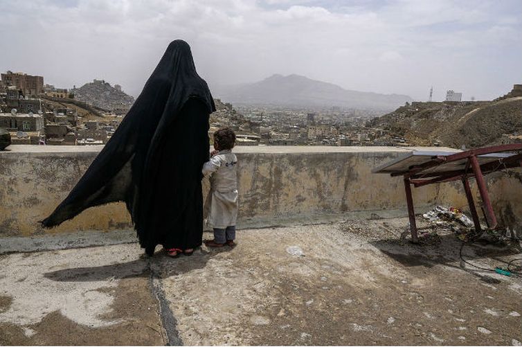 Uma mulher deslocada internamente e sua filha olham a cidade de Sanaa, no Iêmen, a partir do telhado do prédio onde estão abrigadas