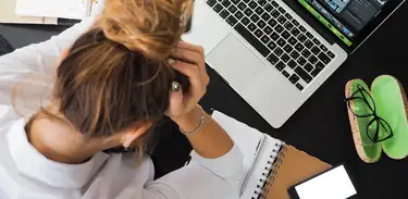 Mulher segura a cabeça em demonstração de cansaço em frente ao computador