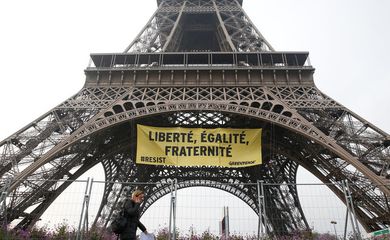 Uma mulher passa pela Torre Eiffel enquanto ativistas do Greenpeace abrem um faixa gigante com 