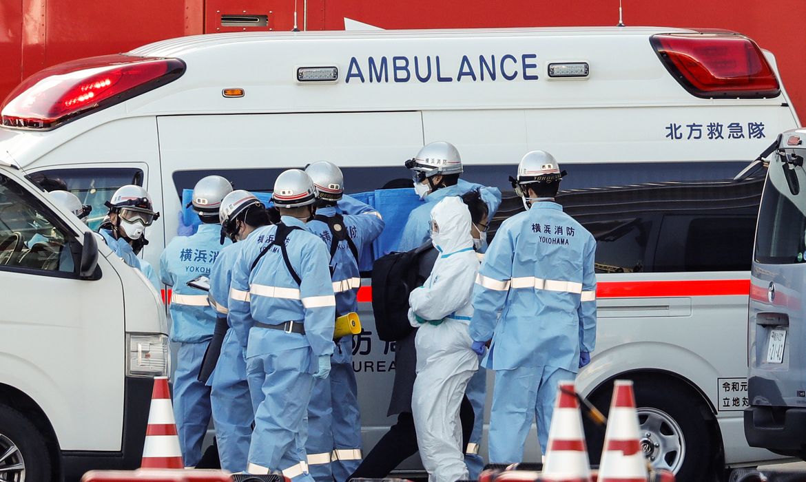 Firefighters wearing protective gear hold canvas up to the windows of an ambulance to protect the privacy of passengers, who tested positive for coronavirus, before they are transferred from the cruise ship Diamond Princess to a hospital, after