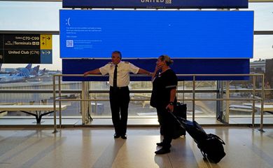 Funcionários da companhia aérea United aguardam à frente de painel de decolagens que mostra uma tela azul de erro, conhecida como 