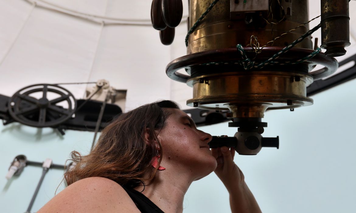 Mulher cientista observa equipamento óptico em observatório astronômico, utilizando telescópio para pesquisa científica e estudos em astronomia no Brasil.