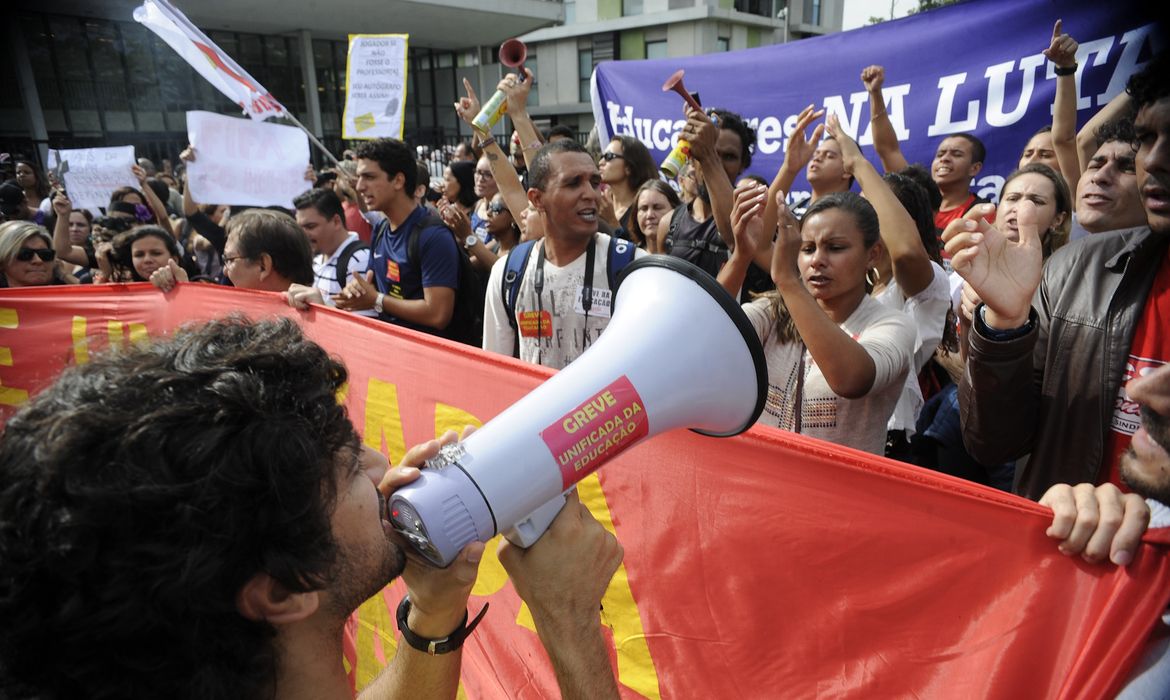 Rio de Janeiro -  Os professores das redes estadual e municipal de ensino do Rio protestam durante a saída do ônibus com parte de jogadores da seleção brasileira, no aeroporto do Galeãoe,  em direção à concentração da equipe na Granja