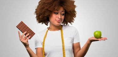 Mulher segura uma barra de chocolate e uma maçã