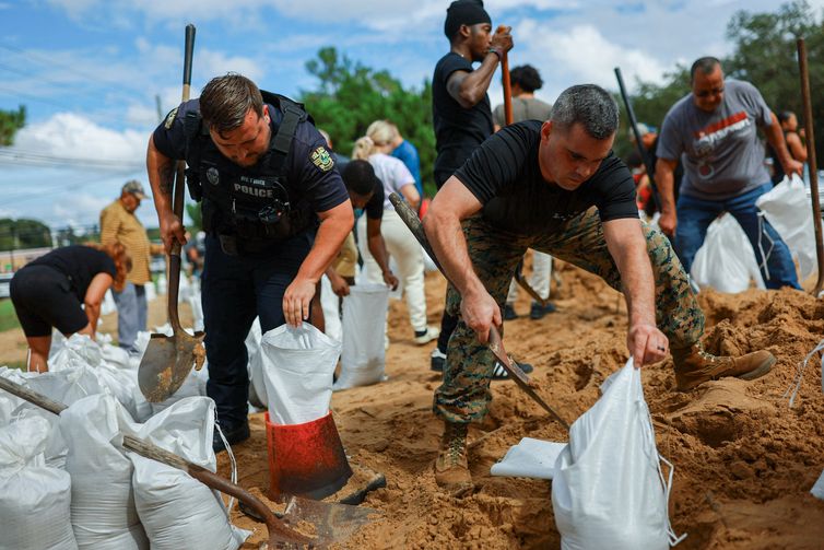 An Orlando Police officer and a U.S. Marine help residents fill sandbags ahead of the arrival of Hurricane Milton, in Orlando, Florida, U.S. October 8, 2024. REUTERS/Jose Luis Gonzalez