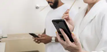 Homem e mulher usam celular no banheiro enquanto escovam os dentes