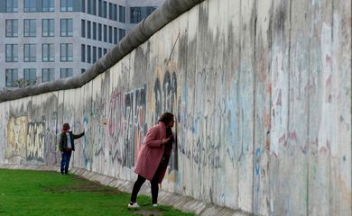 As pessoas tocam os restos do Muro de Berlim no memorial do muro na Bernauer Strasse, em Berlim, Alemanha.