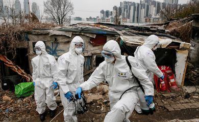 South Korean soldiers in protective gears sanitize shacks as a luxury high-rise apartment complex is seen in the background at Guryong village in Seoul