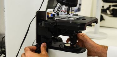 Imagem enquadra mãos de pesquisador enquanto opera um microscópio