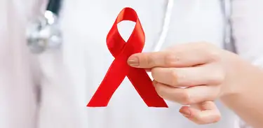 Close e mão de médica segurando laço vermelho – Campanha contra a AIDS