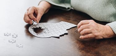 Mulher idosa monta quebra-cabeça em formato de cabeça