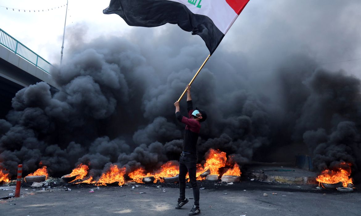 A protester holds an Iraqi flag next to burning tires during ongoing anti-government protests in Kerbala, Iraq November 27, 2019. REUTERS/Abdullah Dhiaa al-Deen