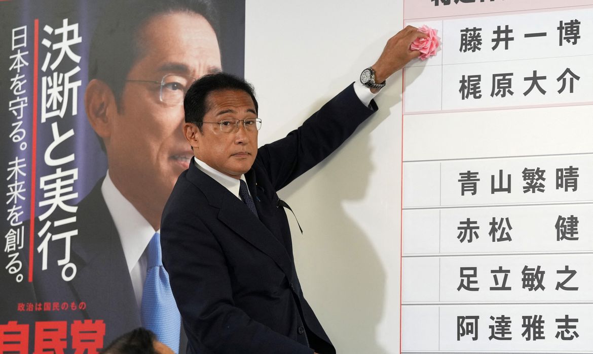 Primeiro-ministro do Japão, Fumio Kishida, coloca papel vermelho ao lado de nomes de candidatos para indicar vitória na eleição para a câmara alta do Parlamento na sede de seu partido em Tóquio