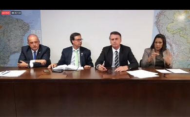 O presidente Jair Bolsonaro faz transmissão ao vivo ao lado do ministro da Casa Civil, Onyx Lorenzoni, do presidente da Embratur, Gilson Machado, e da intérprete de libras, Elizângela Castelo Branco.